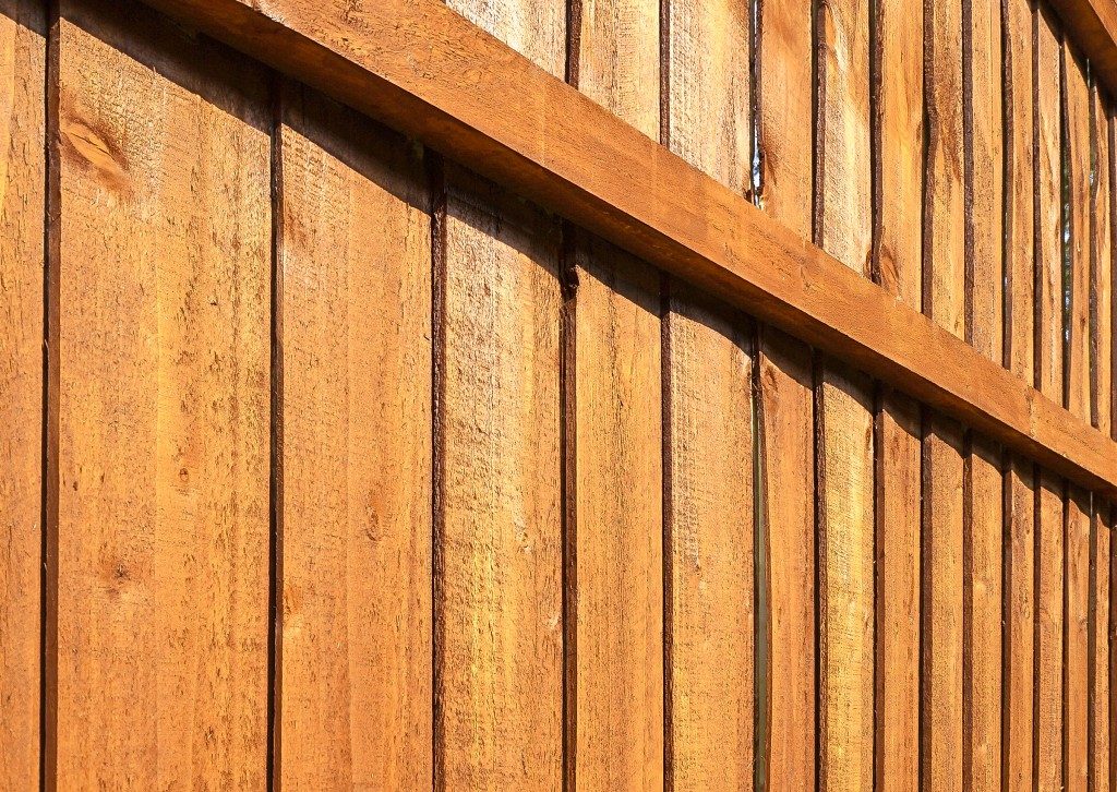 A section of brown, vertical, overlapped wooden garden fence in closeup in the sun with shadows