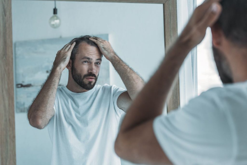 man touching his hair looking in front of the mirror