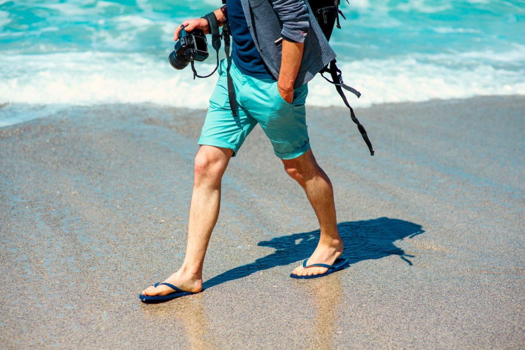 man in shorts holding a camera walking by the shore