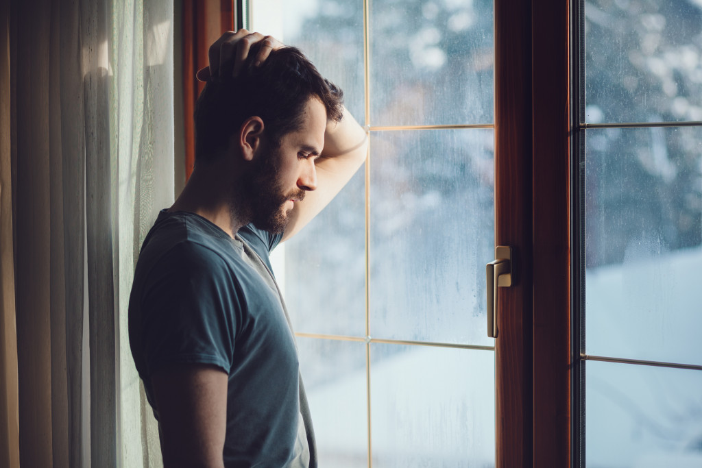 A sad man thinking beside a large window